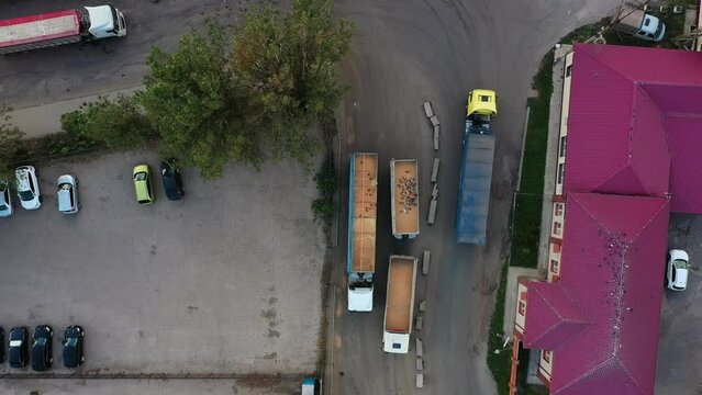 Aerial view from above of grain lorry or dump truck driving through the industrial area of grain elevator silos. Top view of emty body trailer driving along the road. Air drone copter footage.