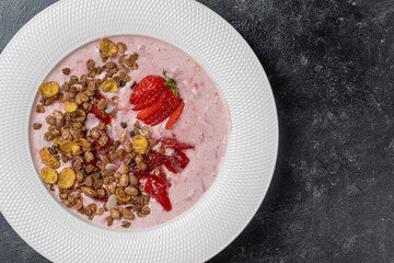 White plate with red strawberries, granola and natural yogurt on a black background, copy space, top view