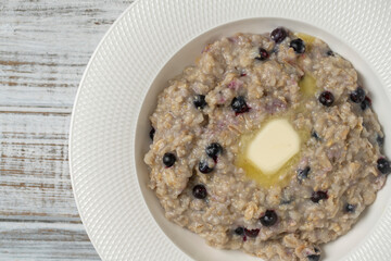 Plain oatmeal porridge with blueberries, butter and honey in white plate