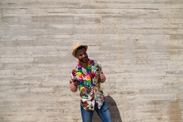 Handsome young man wearing a shirt with Hawaiian flowers, a hat and a necklace with coloured...