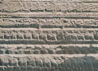 Light beige sand with traces of bicycle treads in the rays of the setting sun. Background with abstract texture.