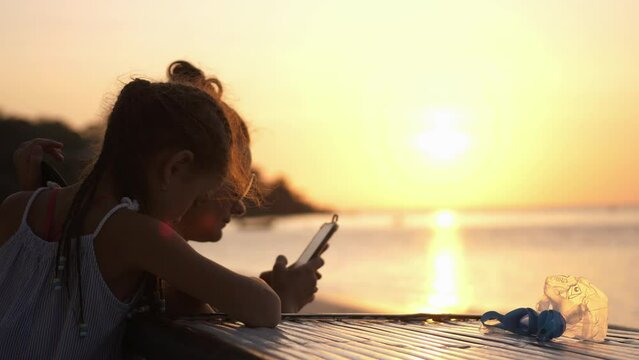 Mother and daughter use mobile phone on the beach at sunset. Concept of technology, lifestyle.