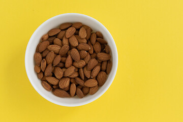 peeled almonds in bowl isolated on yellow background