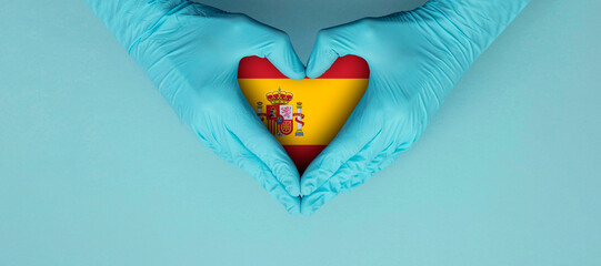 Doctors hands wearing blue surgical gloves making hear shape symbol with spain flag