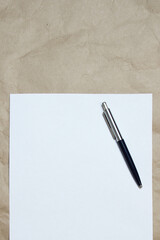 White empty sheet of A4 format with pen on a beige craft paper, vertically oriented. Concept of analysis, study, attentive work. Stock photo with empty place for your text and design.