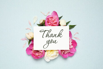 Beautiful peonies and card with phrase Thank You on light blue background, flat lay