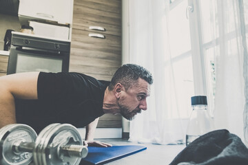 Fototapeta premium Determined sporty young man working out and trains at home. Fit boy doing push-ups exercises on the mat. Strong boy do gymnastics in the living room. Wellness, health, sport, gym, training concept