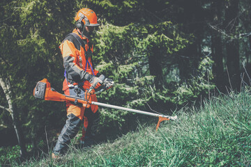 Man holding a brushcutter cut grass and brush. Lumberjack at work wears orange personal protective equipment. Gardener working outdoor in the forest. Security, occupation, forestry, worker, concept