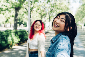 Asian woman taking selfie with girlfriend in park