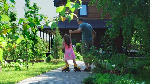 Father and daughter are preparing for roller skating in the fresh air. father's day. The little girl in a beautiful dress learns to roller skating, . High quality 4k footage