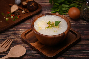 Rice porridge or congee with soft boiled egg, slice ginger and slice scallion topping on wooden table