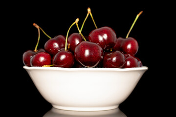 Several sweet cherries with a white ceramic saucer, close-up, isolated on a black background.