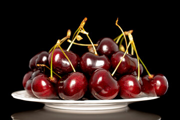 Several sweet cherries with a white ceramic saucer, close-up, isolated on a black background.