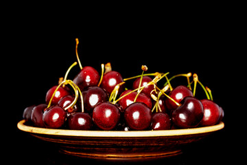Fototapeta na wymiar Several sweet cherries in a ceramic dish, close-up, isolated on a black background.