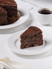 A piece of chocolate cake with apricot jam and chocolate cream on a light table.