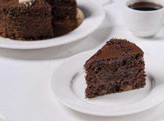 A piece of chocolate cake with apricot jam and chocolate cream on a light table.