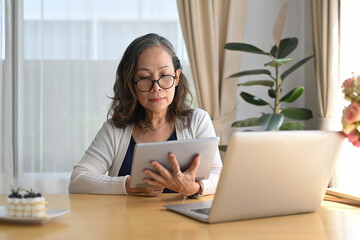 Middle aged woman browsing wireless Internet on tablet at home. Elderly technology concept