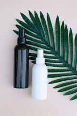 Natural organic eco cosmetics concept. Vertical photo of two spray bottles in white and black colors on beige background with tropical leaf