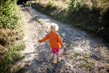 A little girl runs along a rural road in the summer in sunny weather at sunset