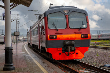 A bright red train pulls up to the platform of the railway station in the city. Passenger Transportation.