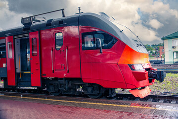Obraz premium A bright red train stands on the platform of the railway station in the city. Passenger Transportation.