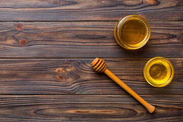 Obraz na płótnie Canvas Glass jar of honey with wooden drizzler on colored background. Honey pot and dipper high above. Top view copy space