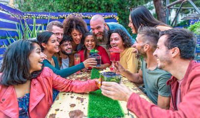 multiethnic group of friends sitting on a table in a lounge bar restaurant making toast with wonderful gourmet cocktail. diverse people celerating together enjoying happy hour on holiday. lifestyle