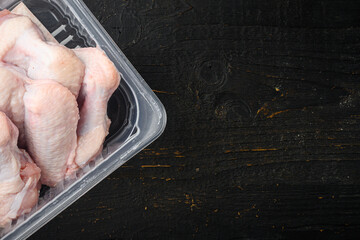 Raw chicken wings in plastic pack, on black wooden table background, top view flat lay, with copy space for text