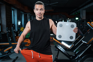 young attractive athlete male weight with scale in gym and dieting