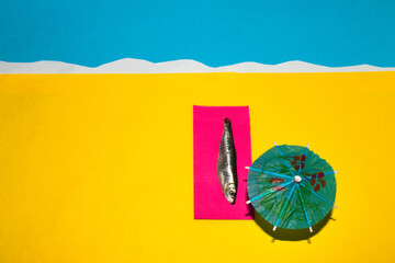 fish on the sandy beach lies on the purple deck chair and the sunbathing is next to the umbrella,...
