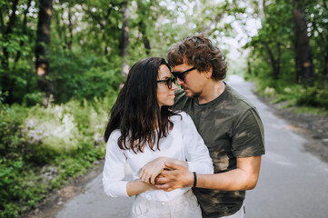 Beautiful, stylish bearded man and hippie brunette woman in sunglasses hugging and smiling outdoors in the park. Portrait, photograph of people in love.
