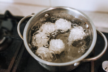 Chicken white eggs are boiled in boiling water in a metal saucepan.