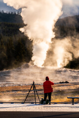 Tourist taking the explosion of old Faithful, Yellowstone in morning.