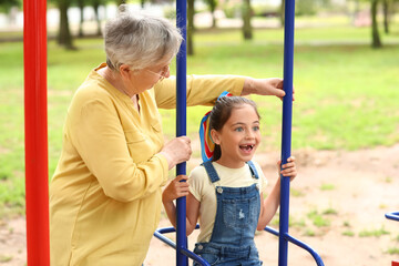 Little girl with her grandma playing on swings in park