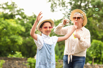 Little girl and her grandma blowing soap bubbles in park