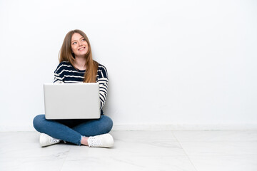 Young caucasian woman with a laptop sitting on the floor isolated on white background looking up...