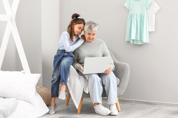 Little girl and her grandma using laptop in bedroom