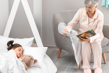 Senior woman reading bedtime story to her little granddaughter in bedroom