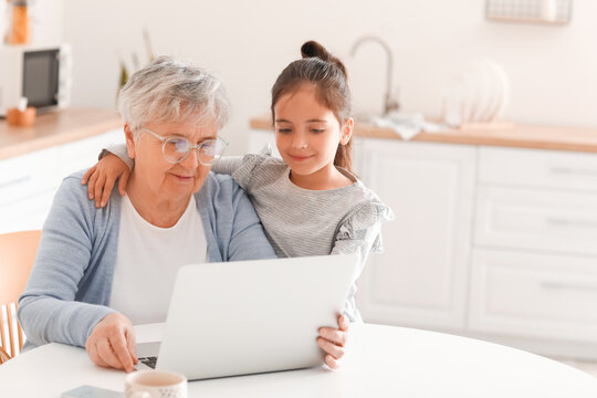Little girl with her grandma using laptop in kitchen