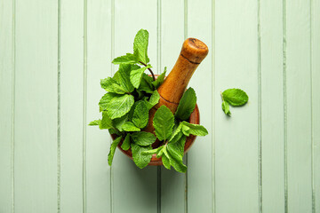 Mortar and pestle with mint leaves on color wooden background
