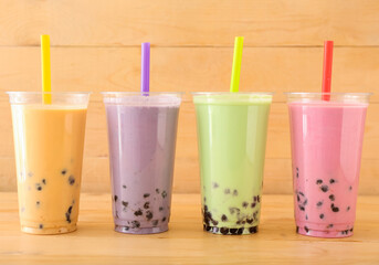 Plastic cups of different tasty bubble tea on wooden background