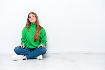 Young caucasian woman sitting on the floor isolated on white background and looking up