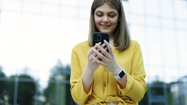 Appealing young elegant caucasian woman using social media application on smartphone text messages receive news smiling outdoor. People portraits and technology concept