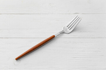 Stylish stainless steel fork on white wooden background