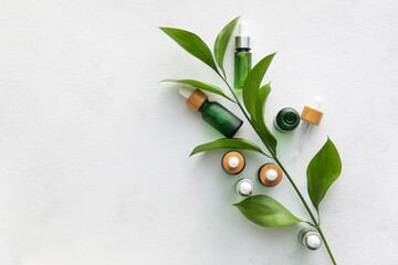 Bottles of natural serum and plant leaves on light background