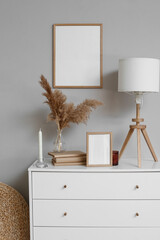 Chest of drawers with frames, vase, books and lamp near grey wall