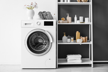 Washing machine, flowers in vase, shelving unit with bath accessories near black and white wall