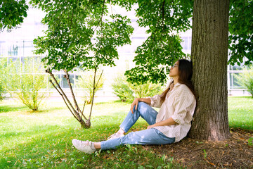 Young Asian Thai, Vietnamese or Chinese woman in oversize shirt, jeans and glasses sitting relaxing...