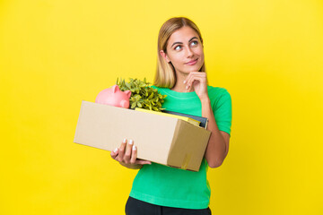 Young Uruguayan girl making a move while picking up a box full of things isolated on yellow...
