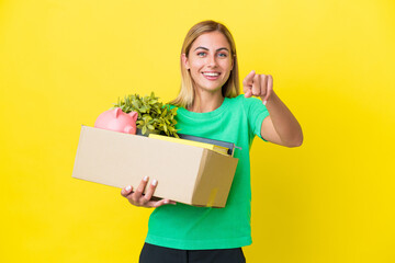 Fototapeta na wymiar Young Uruguayan girl making a move while picking up a box full of things isolated on yellow background pointing front with happy expression